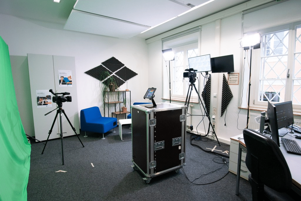 Modernes Video-Studio mit professioneller Ausrüstung: Kamera auf Stativ, Beleuchtung, Monitor, Schallschutzplatten und Arbeitsplatz mit Computer. Perfekt für Videoproduktionen und Streaming.